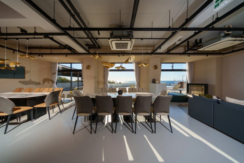 海を一望できる広々としたモダンなダイニング兼リビングルーム。スタイリッシュな家具が配置され、窓から差し込む自然光が明るい雰囲気を演出しています。