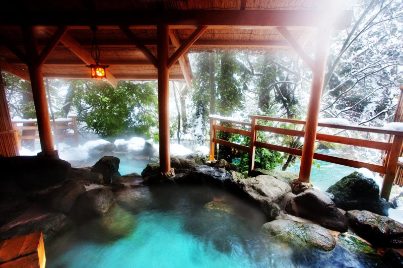 雪が積もる冬の情景の中、湯気が立ち上る露天風呂