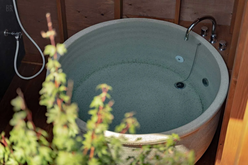 木製の壁に囲まれた丸い石造りの露天風呂