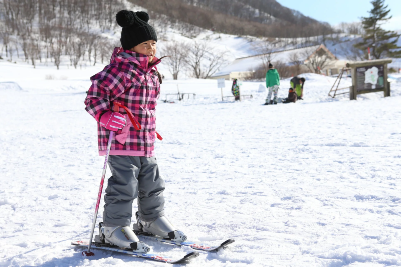ピンクのスキーウェアを着てスキー板とストックを持つ女の子