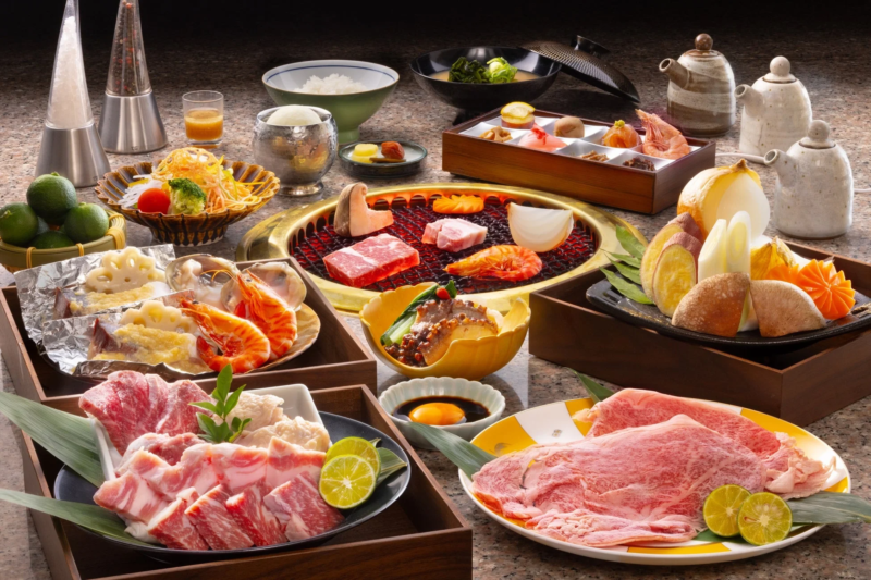 新鮮な肉、海鮮、野菜が豪華に盛り付けられた日本の焼肉料理の全景です。中央の焼き網には牛肉やエビ、玉ねぎなどが置かれ、食欲をそそる豊かな食卓が広がっています。特別な日の食事に最適なご馳走です。