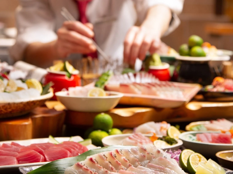 料理人が様々な種類の新鮮な刺身や海鮮料理を準備している様子が写っています。マグロや白身魚などが美しく盛り付けられ、ライムが添えられています。日本の伝統的な食文化を感じさせる一枚です。