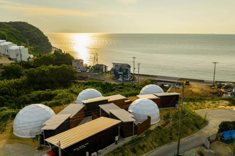 夕焼けに染まる海を望むグランピング施設の空撮
