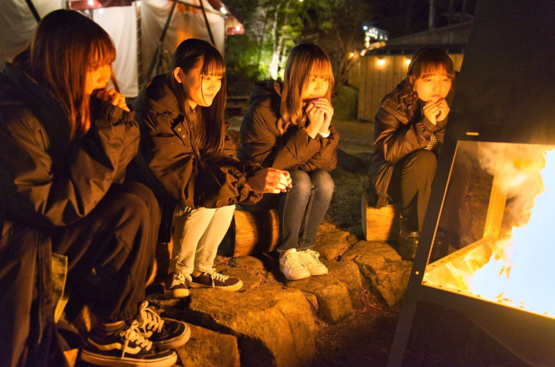 若い女性が焚き火を囲んで暖をとっている様子