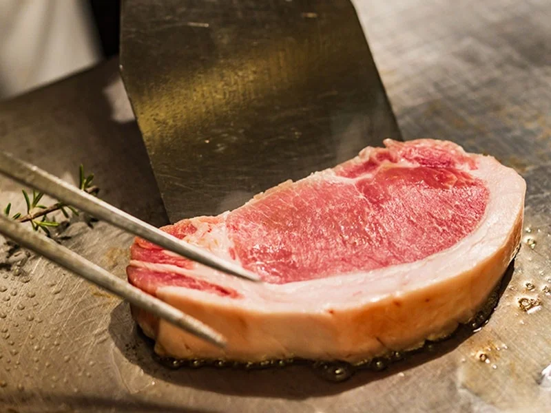 熱した鉄板の上で厚切りの生肉が焼かれている様子を捉えた画像です。