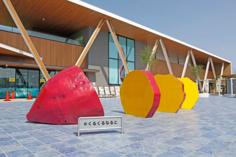 青いタイル張りの広場に、巨大なさつまいもを模した赤と黄色のカラフルなモニュメントが並んでいます。