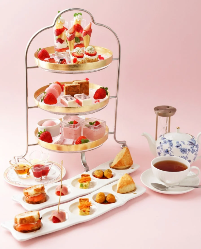 ピンクの背景に、3段のスタンドに盛り付けられた苺尽くしのスイーツやセイボリー、そして紅茶が並ぶ、華やかなアフタヌーンティーの様子。