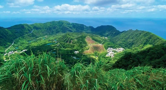 青い空と海を背景に、緑豊かな山々と谷が広がる壮大な島の風景