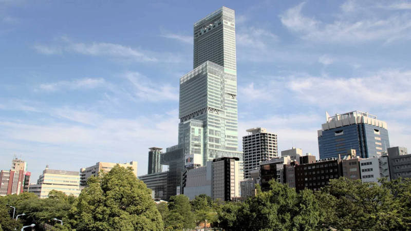 大阪の都市景観を捉えた一枚。青空の下、そびえ立つあべのハルカスを中心に、近代的なビル群と手前の豊かな緑が調和した風景が広がっています。