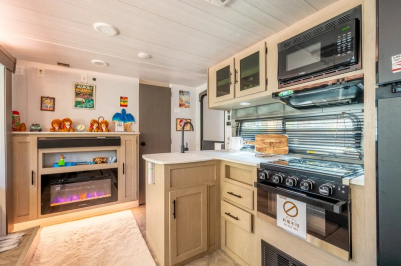 キャンピングカー、RV、キッチン、リビングルーム、暖炉、電子レンジ、オーブン、シンク、キャビネット、コンパクト、室内、家具、ぬいぐるみ、ポスター、窓、ブラインド