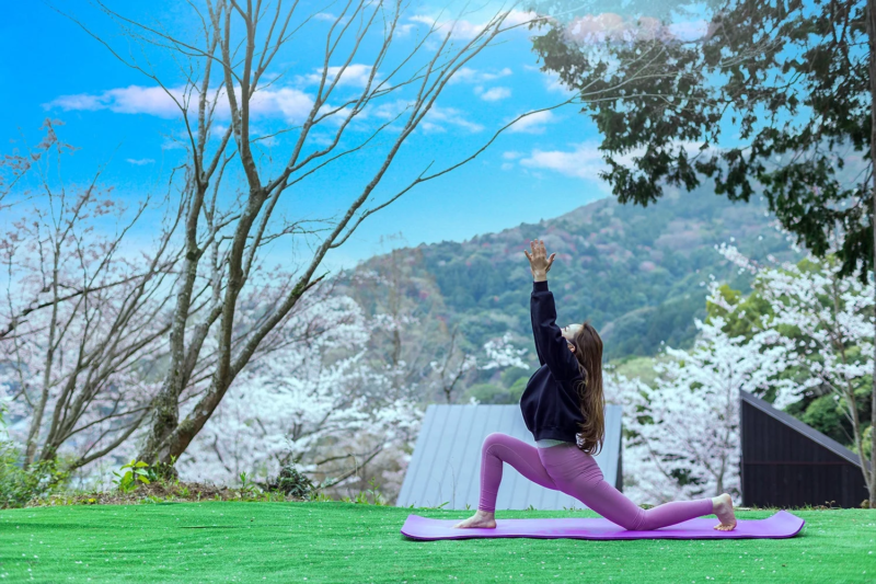 春の美しい自然の中で、女性がヨガマットの上で桜を背景にヨガのポーズをとっています
