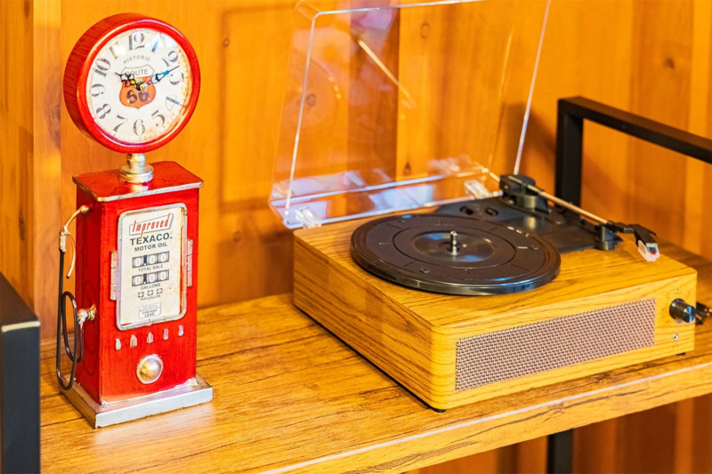 木製の棚に置かれた、レトロなデザインのレコードプレーヤーと、赤いガソリンスタンド型置時計の様子