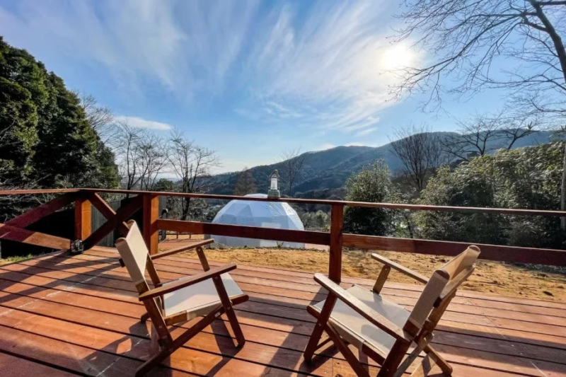 木製のデッキに置かれた2脚の椅子から、ドーム型テントや山々を見下ろす景色