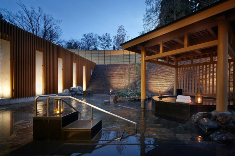 モダンなデザインの露天風呂で、夜の静寂が漂う癒しの空間。木材と石が調和し、柔らかな照明が心地よい雰囲気を演出しています。