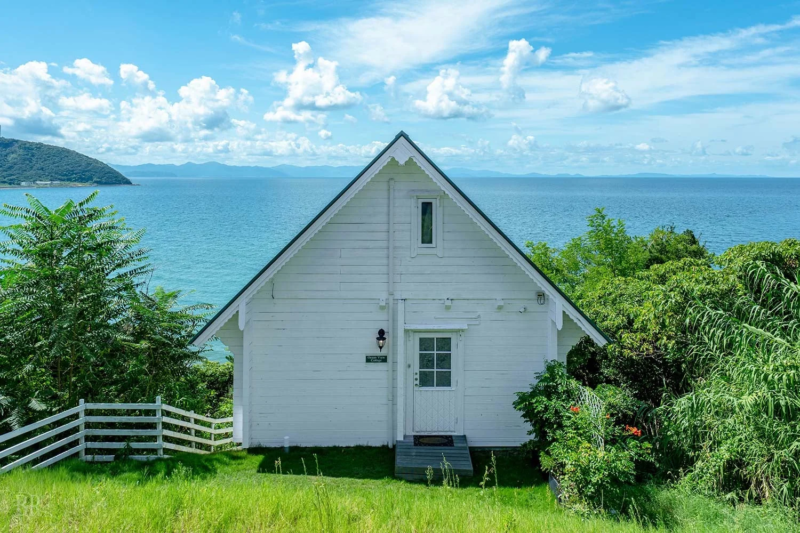 青い海と空が広がる海岸に建つ、白いコテージ