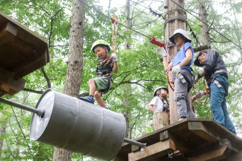森林のアドベンチャーパークで樽を渡る子供
