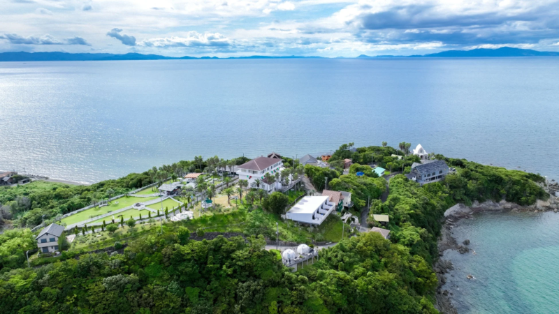 青い海に突き出した緑豊かな岬を空撮した画像