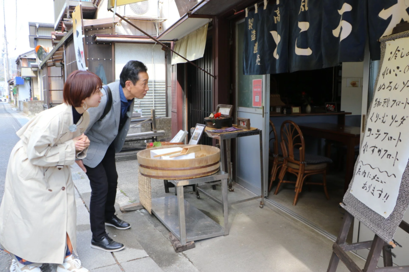 昔ながらの商店の前でメニューを眺める男女