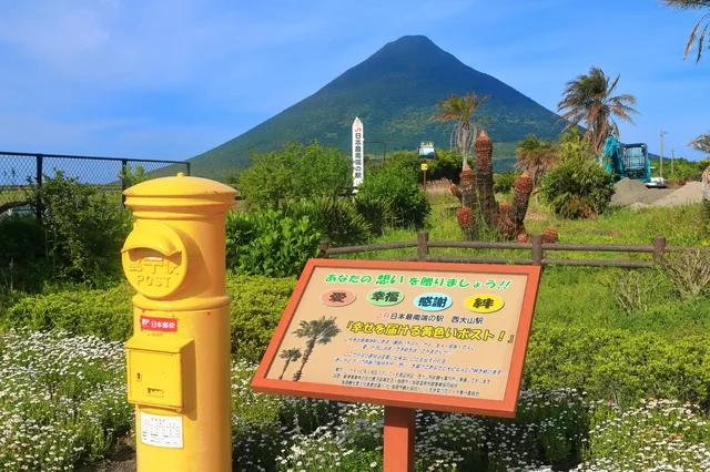 JR日本最南端の駅、西大山駅に設置された「幸せを届ける黄色いポスト」と、その背景にそびえる開聞岳の美しい風景