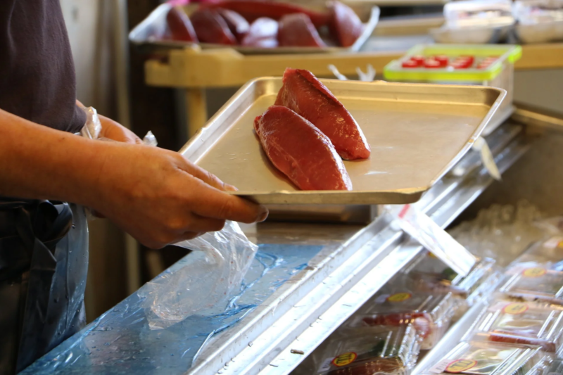 鮮魚店でカツオの切り身を運ぶ店員