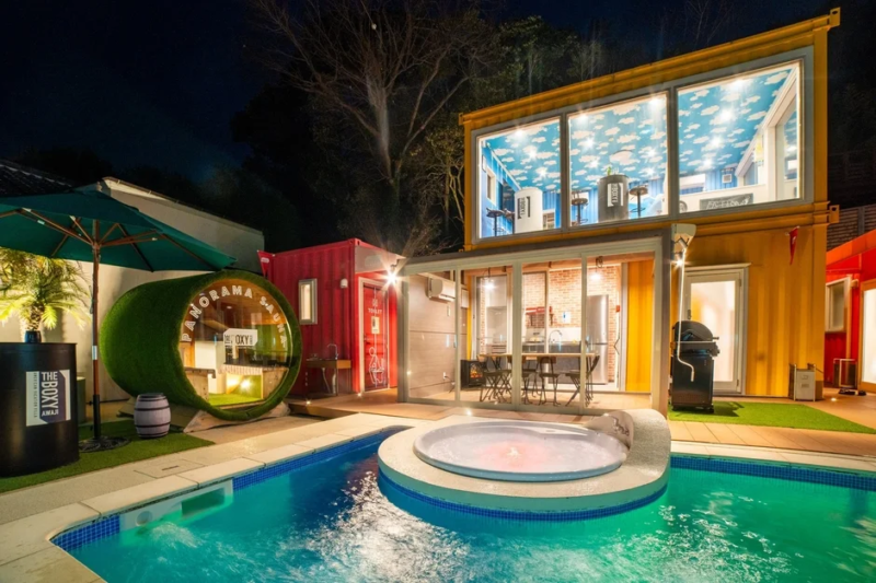 夜間にライトアップされた、コンテナハウス型のモダンな宿泊施設です。プール、ジャグジー、パノラマサウナを備え、リゾート感あふれる空間が特徴です。