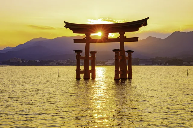 厳島神社の大鳥居が海に浮かび、夕日または朝日が鳥居の間から輝いている美しい風景