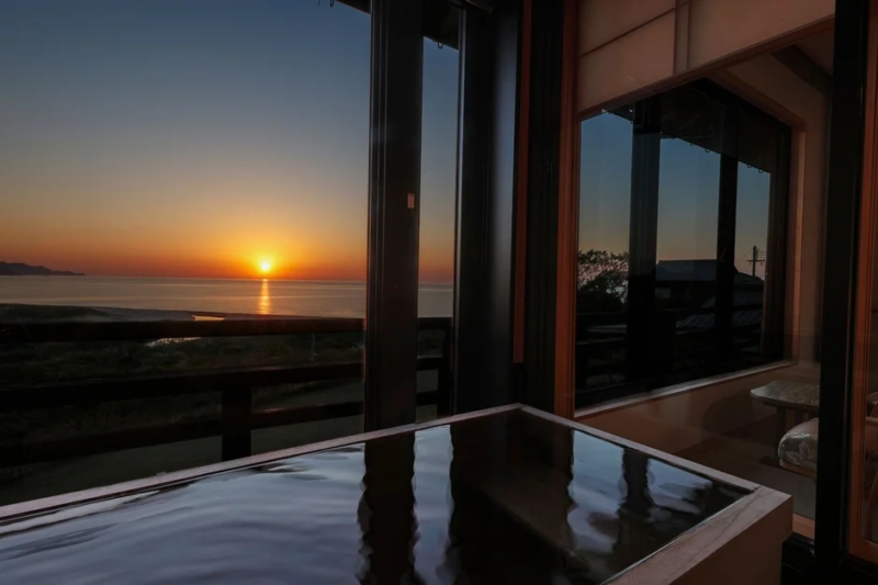 海に沈む夕日を望む窓辺に、水面が波打つ浴槽が配された贅沢な空間
