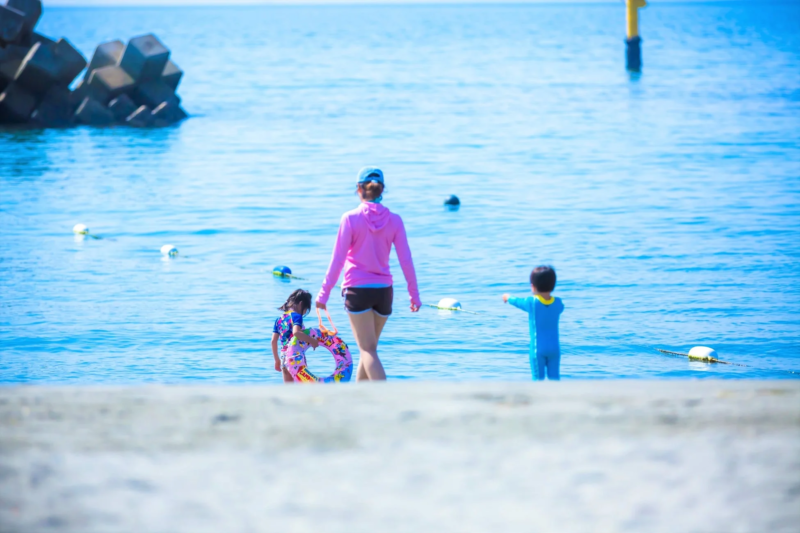 晴れた日の海辺で、母親と二人の子供が水遊びを楽しんでいる様子