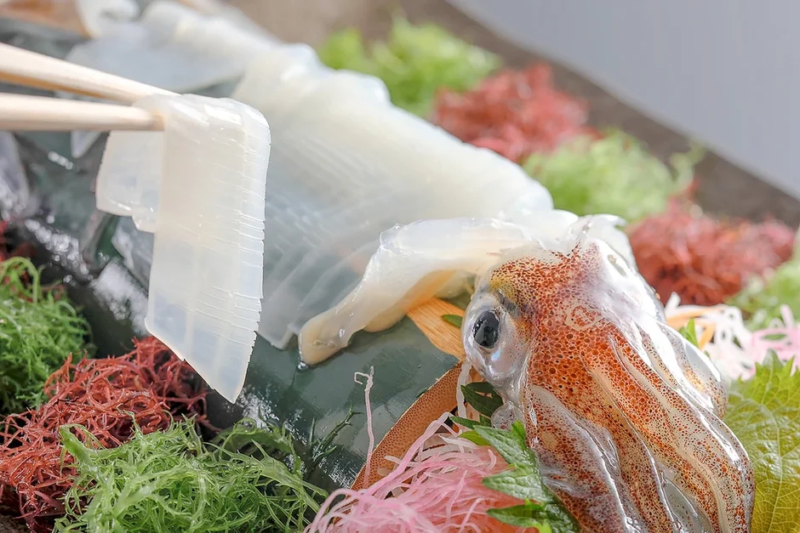 箸でつまみ上げられた新鮮なイカの刺身