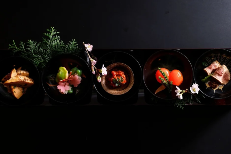 黒い背景に、黒い漆器に盛り付けられた色とりどりの会席料理