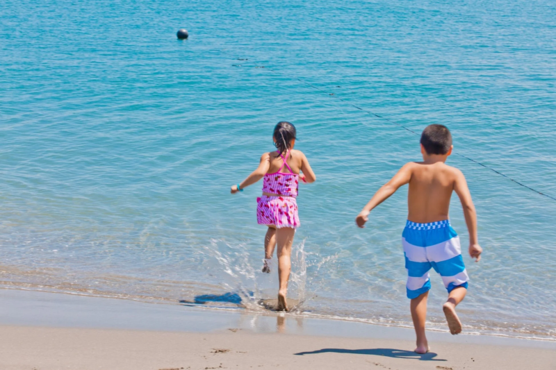 晴れた日に、水着姿の少年と少女が青い海に向かって楽しそうに駆け込んでいる様子