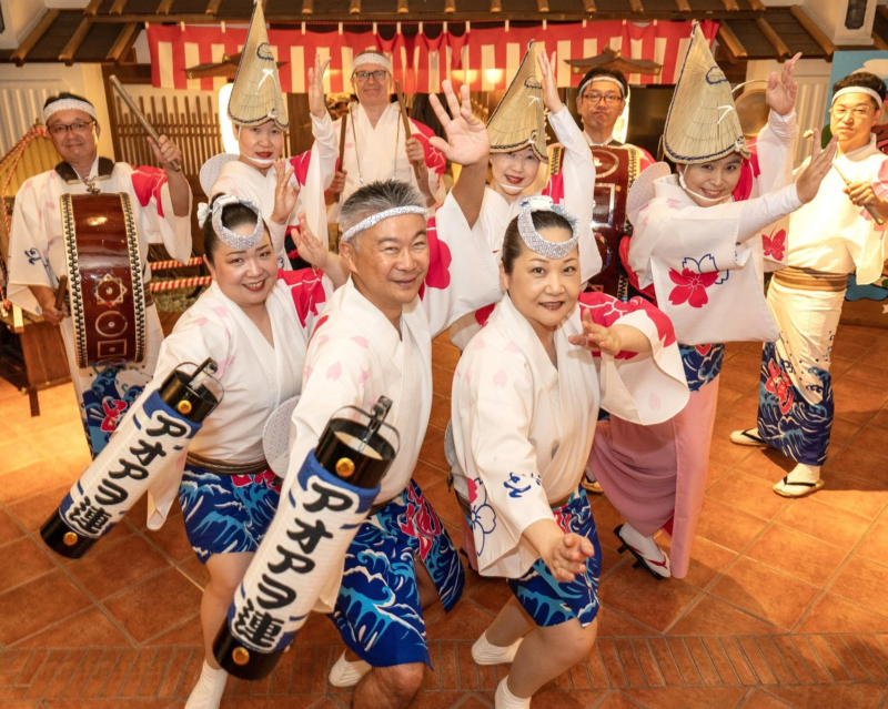 日本の伝統的な祭りの衣装をまとった人々が、笑顔で阿波踊りのポーズをとっています