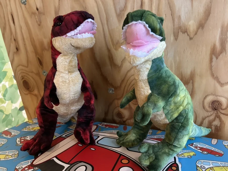 赤いチェック柄と緑色のティラノサウルスのぬいぐるみが並ぶ