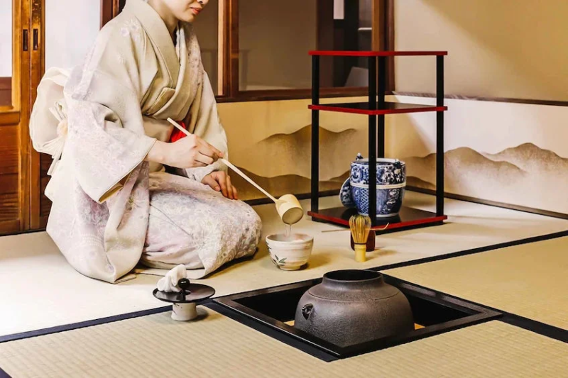 着物を着た女性が和室で茶道を披露している様子です。畳敷きの空間には炉が設けられ、柄杓で茶碗にお湯を注ぐ瞬間が捉えられています。日本の伝統文化を感じさせる静謐な一枚です。