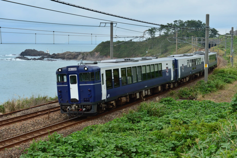 JR 青と白の列車が海岸沿いの鉄道を走行している