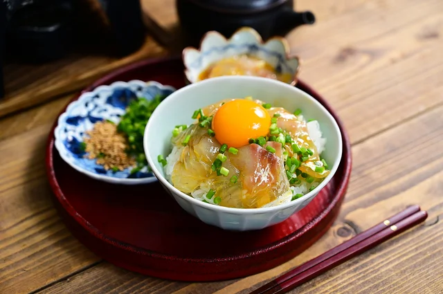 ご飯と新鮮な魚の切り身、卵黄、青ネギが盛り付けられた和風の丼物