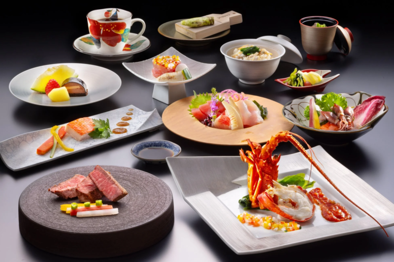 豪華な和食の会席料理が多数並べられた一枚。新鮮な刺身、ロブスター、ステーキ、煮物、デザートなど、彩り豊かな品々が美しく盛り付けられ、贅沢な食事の雰囲気を伝えています。