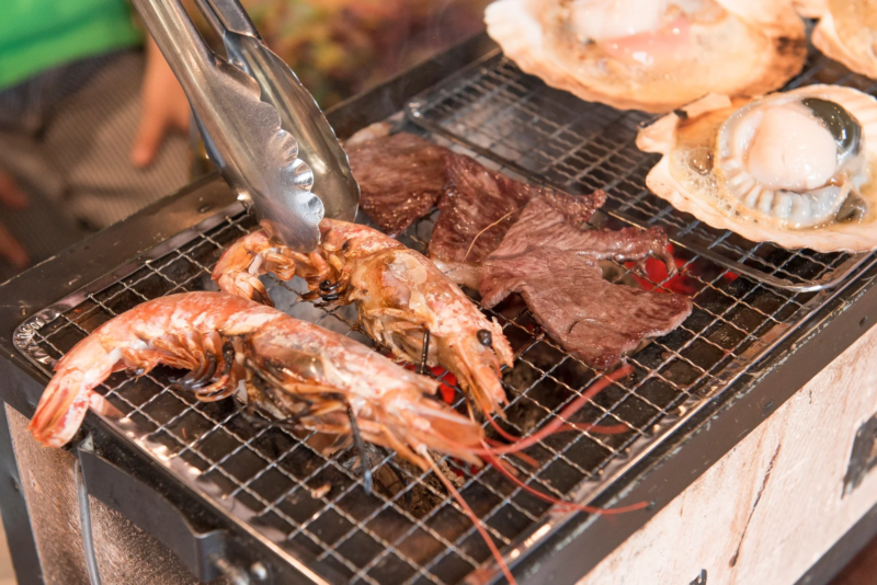 網の上で焼かれるエビ、牛肉、ホタテなどの食材