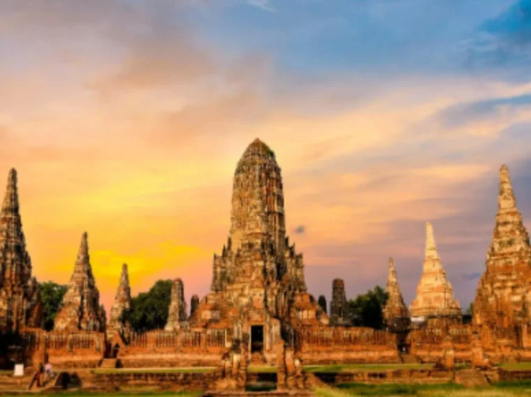 夕焼け空を背景に、タイのアユタヤにあるワット・チャイワッタナラム寺院の壮大な遺跡が写っています。中央には大きな塔があり、その周りに複数の小さな仏塔が配置されています。歴史と美しさを感じさせる風景です。